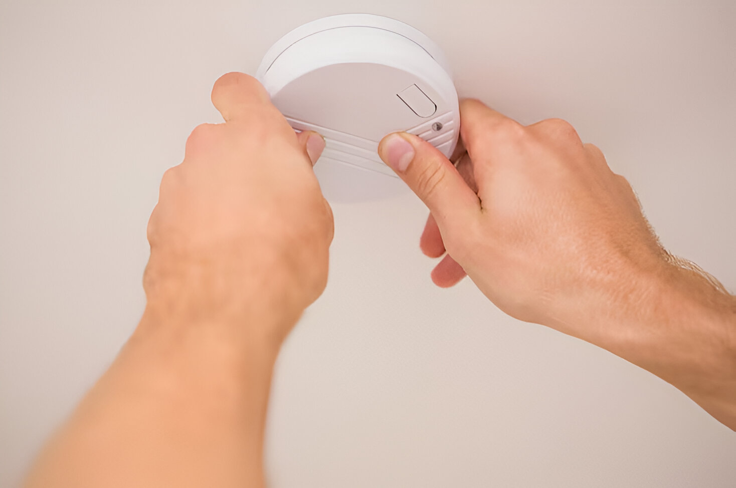 A person uses both hands to supply & install new smoke alarms, testing them on the ceiling for safety.