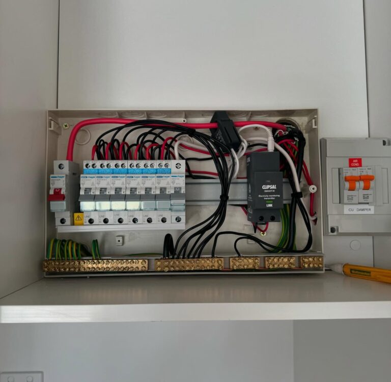 An open electrical distribution board with circuit breakers, wiring, a surge protector, and a safety switch installed, mounted on a white wall—a prime example of professional Safety Switch Installation Inner West.