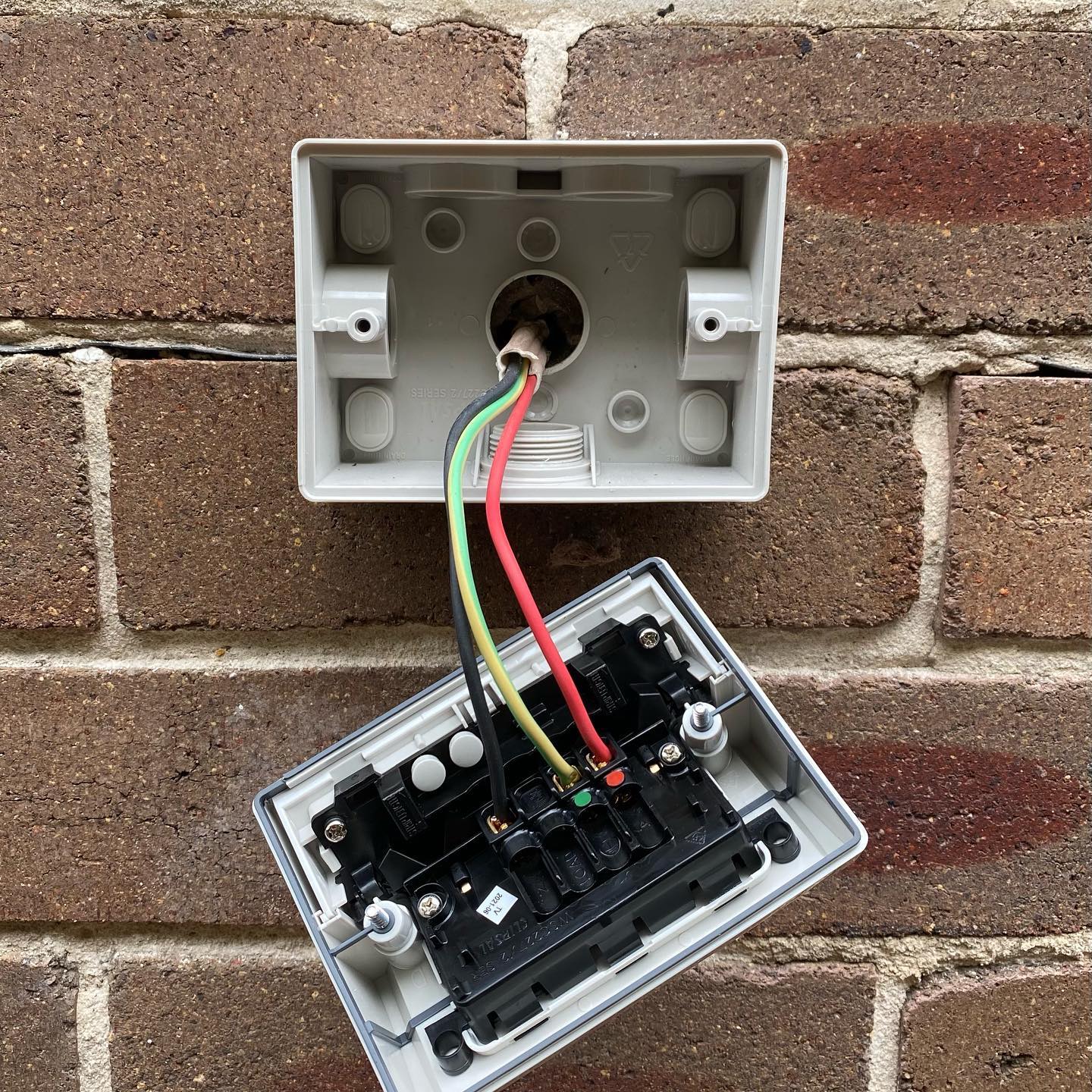 An open outdoor electrical box mounted on a brick wall reveals exposed red, black, green, and yellow wires connected to terminals—highlighting the need to upgrade old or damaged power points for improved safety.