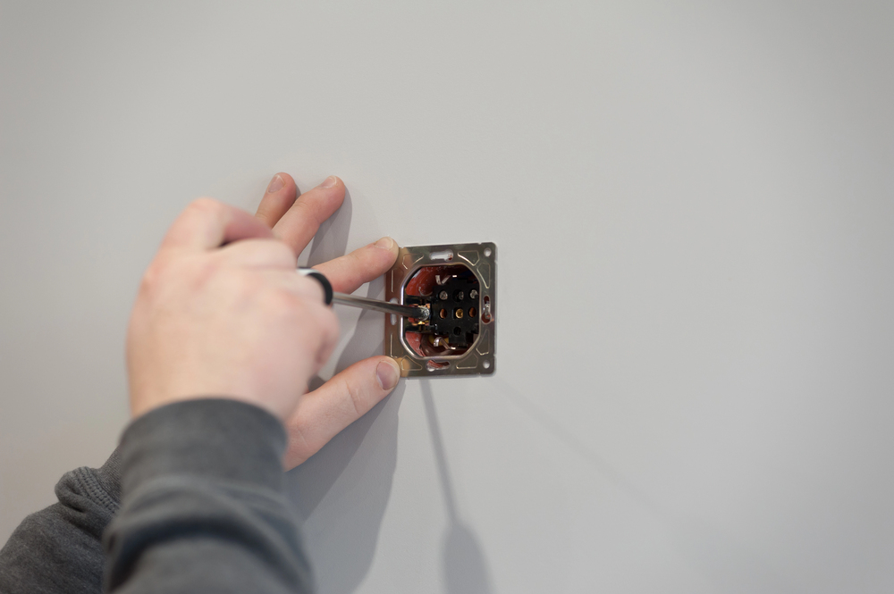 Using a screwdriver to install a kinetic switch into a metal mounting frame on a plain white wall.